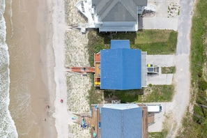 An aerial view of a beachside property with a large blue-roofed building, a smaller structure with a red roof, and a sandy beach with a few people. - Dog-friendly oceanfront escape (North Topsail Beach)