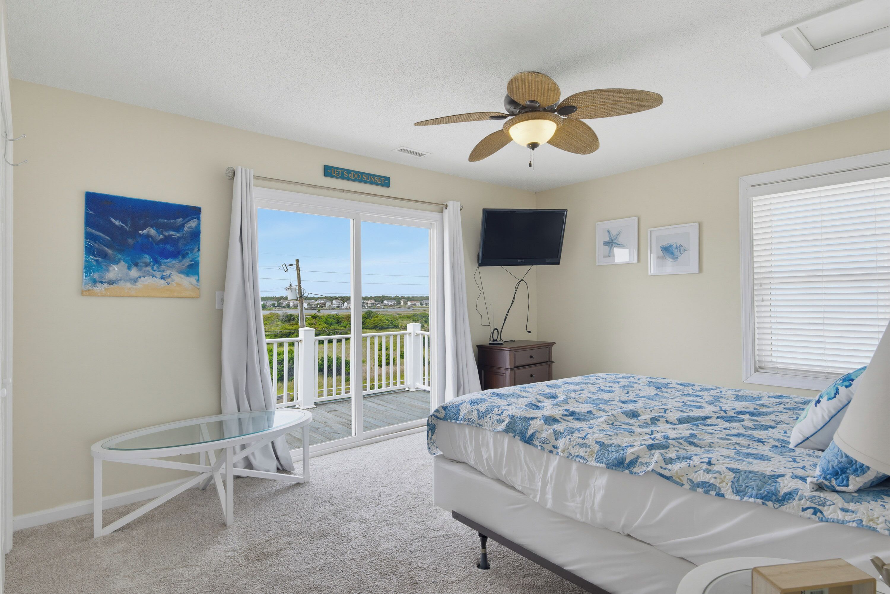 A bedroom with a bed, a ceiling fan, a television, and a view of the outdoors.