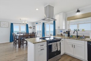 A modern kitchen with white cabinets, a central island, and a view of the sea through large windows. - Dog-friendly oceanfront escape (North Topsail Beach)