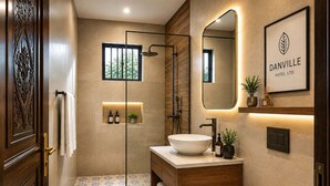 Een moderne badkamer met een groot wastafel, toilet en douche. Er hangt een spiegel boven de wastafel en een logo in een lijst op de muur.