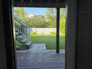 En träveranda som leder ut till en gräsklädd trädgård med ett vitt staket och en trappa.