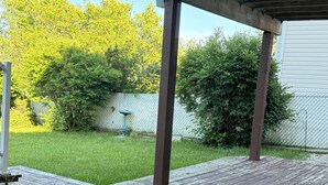 Um deck de madeira com estrutura de pérgola, rodeado por um gramado e uma cerca de arame.