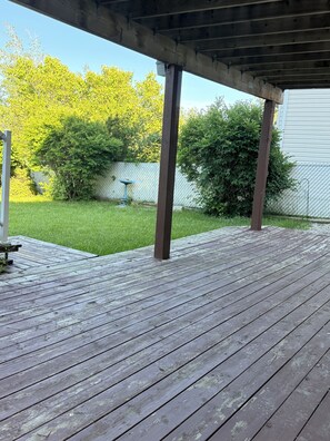 Ett trädäck med en pergola, omgivet av en gräsyta och ett stängsel av sammanlänkade metallkedjor.