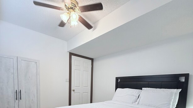 A bedroom with a bed, a ceiling fan, a wardrobe, and a door.