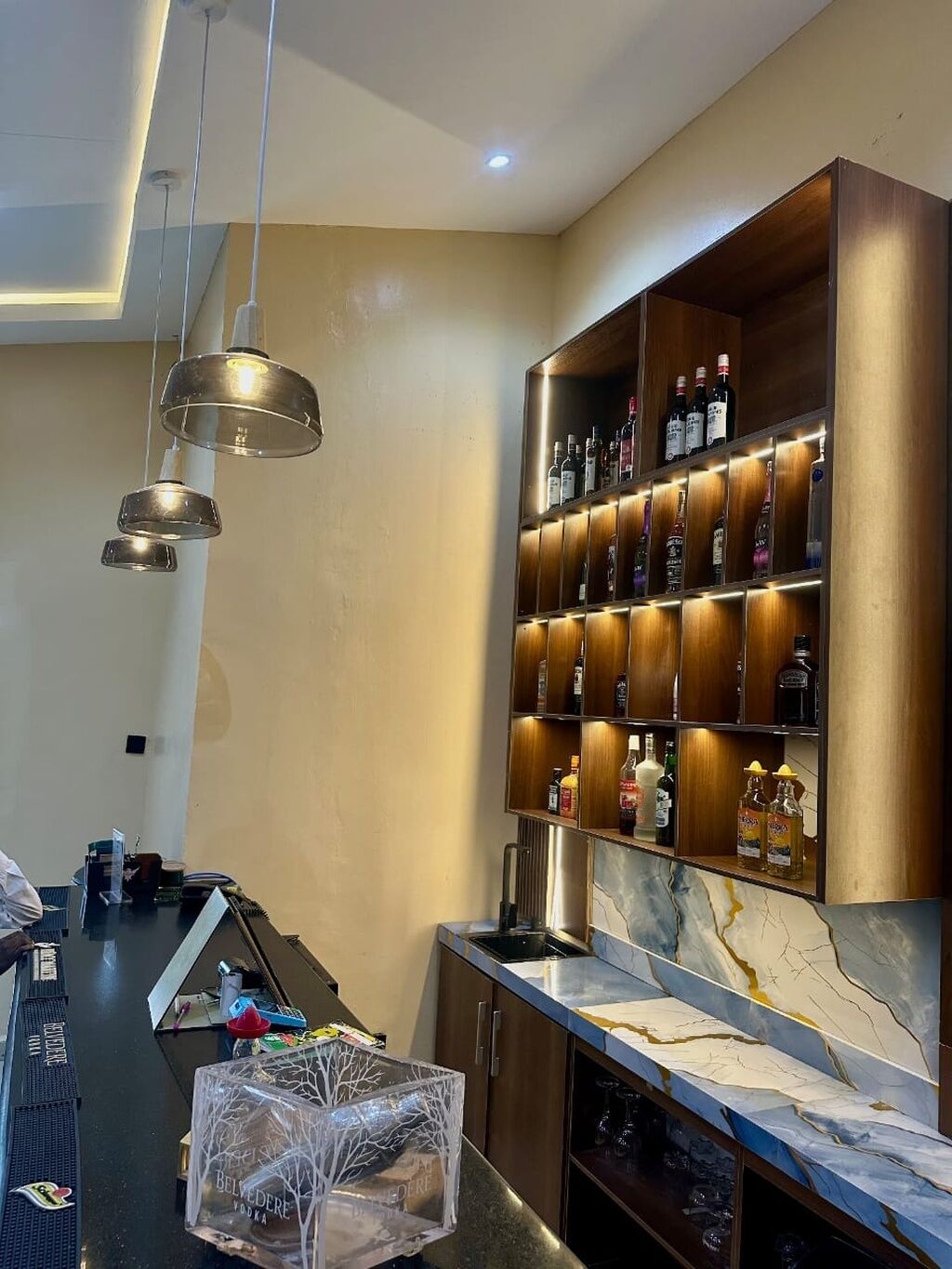 Zona de bar con mostrador de mármol y estanterías llenas de botellas de licores.