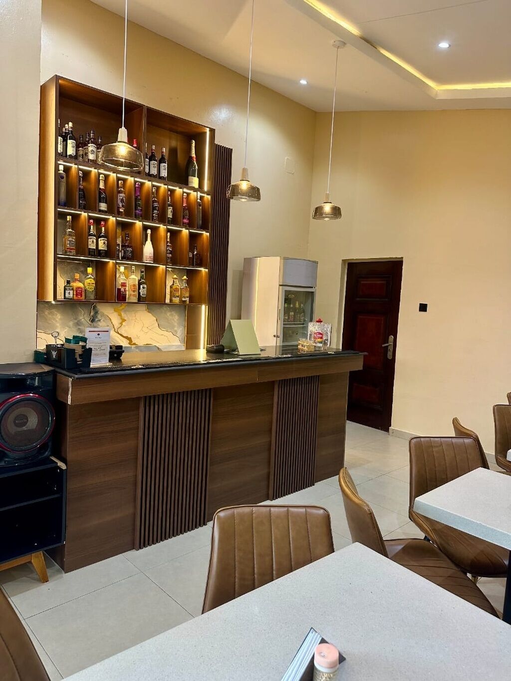 A bar area with a wooden counter, shelves of liquor bottles, and hanging pendant lights.
