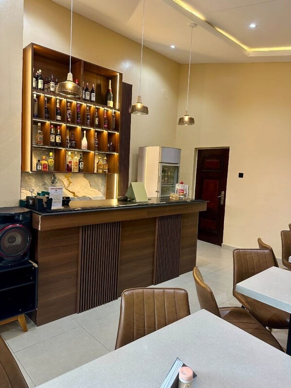 A bar area with a wooden counter, shelves of liquor bottles, and hanging pendant lights. - RT24 Hotel (Lagos)