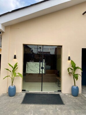 A hotel entrance with a glass door, two potted plants, and a black mat at the entrance. - RT24 Hotel (Lagos)