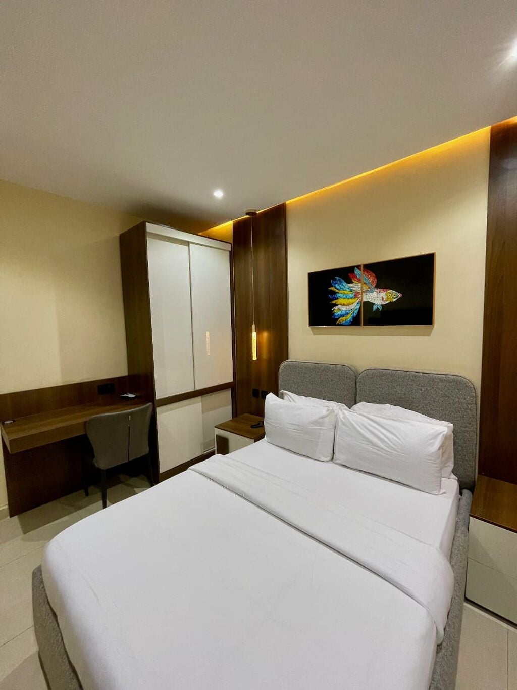 Ein Hotelzimmer mit Bett, Schreibtisch, Kleiderschrank und einem an der Wand hängenden Kunstwerk.