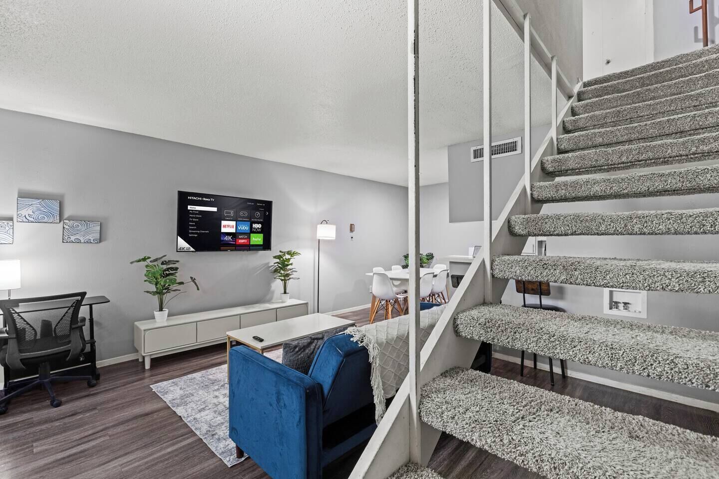 A modern living room with a flat-screen TV, a dining area, and a staircase.