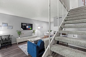 A modern living room with a flat-screen TV, a dining area, and a staircase. - Cozy 1BR in a convenient Austin location. (Austin)