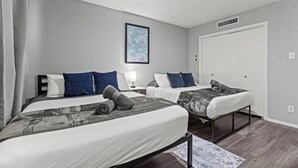 Et hotelværelse med to senge, et natbord med en lampe, et billede i ramme på væggen og en dør med et vindue.