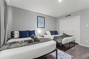 A hotel room with two beds, a bedside table with a lamp, a framed artwork on the wall, and a door with a window. - Cozy 1BR in a convenient Austin location. (Austin)