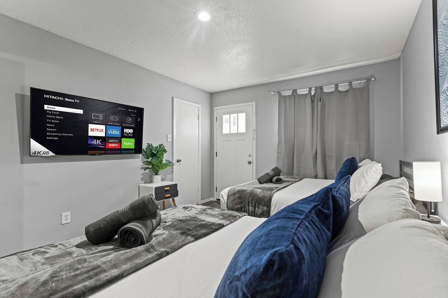 A hotel room with a flat-screen TV displaying streaming services, a bed with a headboard, a bedside table with a lamp, and a window with curtains.