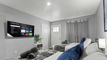 A hotel room with a flat-screen TV displaying streaming services, a bed with a headboard, a bedside table with a lamp, and a window with curtains.