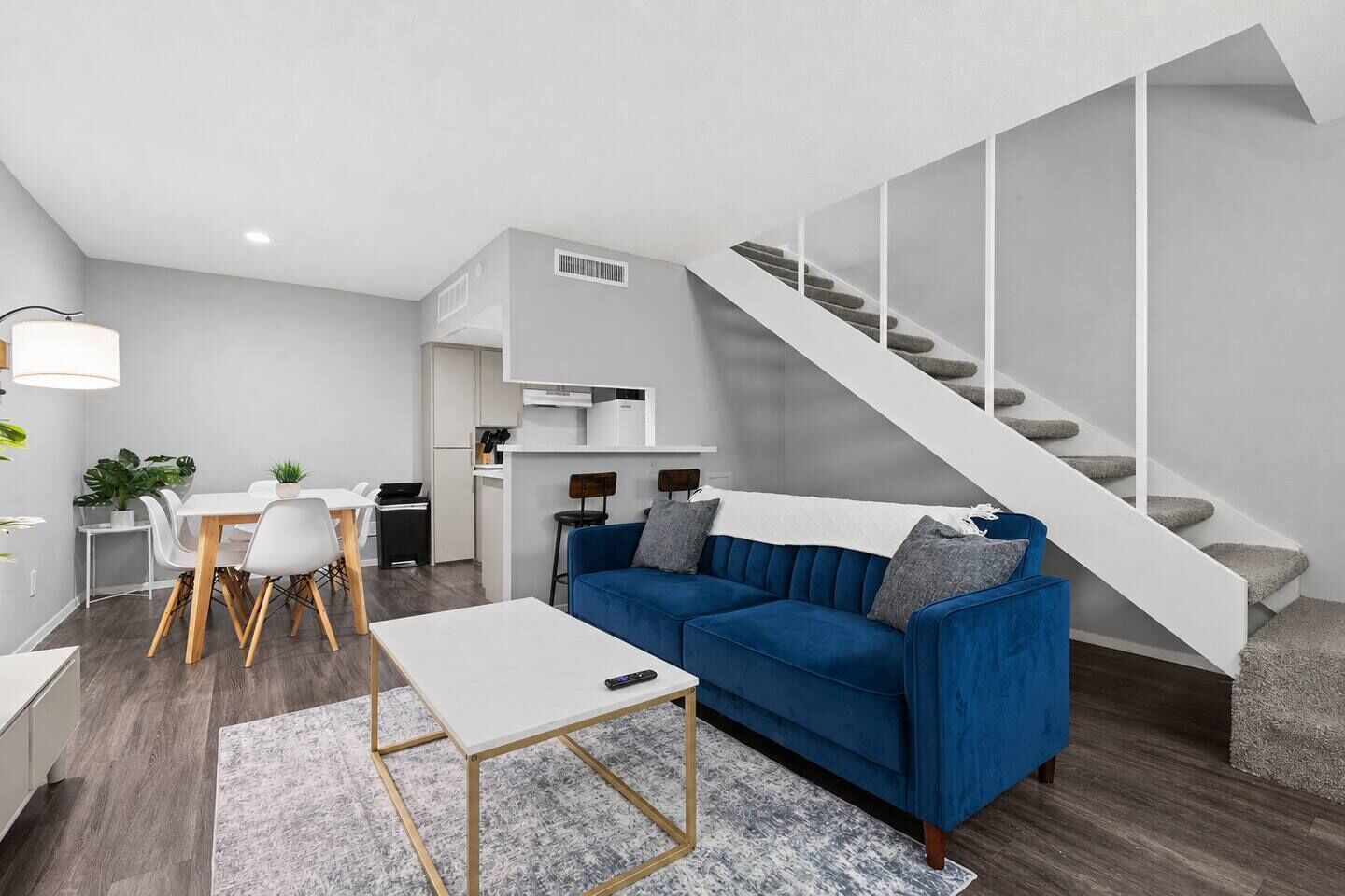 Un salon moderne avec un canapé bleu, une table basse blanche et un escalier.