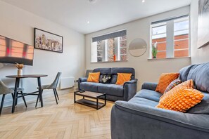 A modern living room with a grey sofa set, a coffee table, and a dining area with a round table and chairs. - Modern Flat In Jewellery Quarter Free Parking (Birmingham)