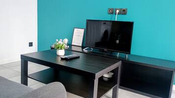 A modern living room with a flat-screen TV, a coffee table, a potted plant, and a framed certificate on the wall.