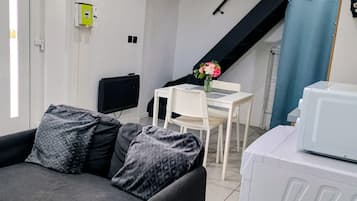A modern living room with a sofa, a flat-screen TV, a dining table with chairs, and a staircase.