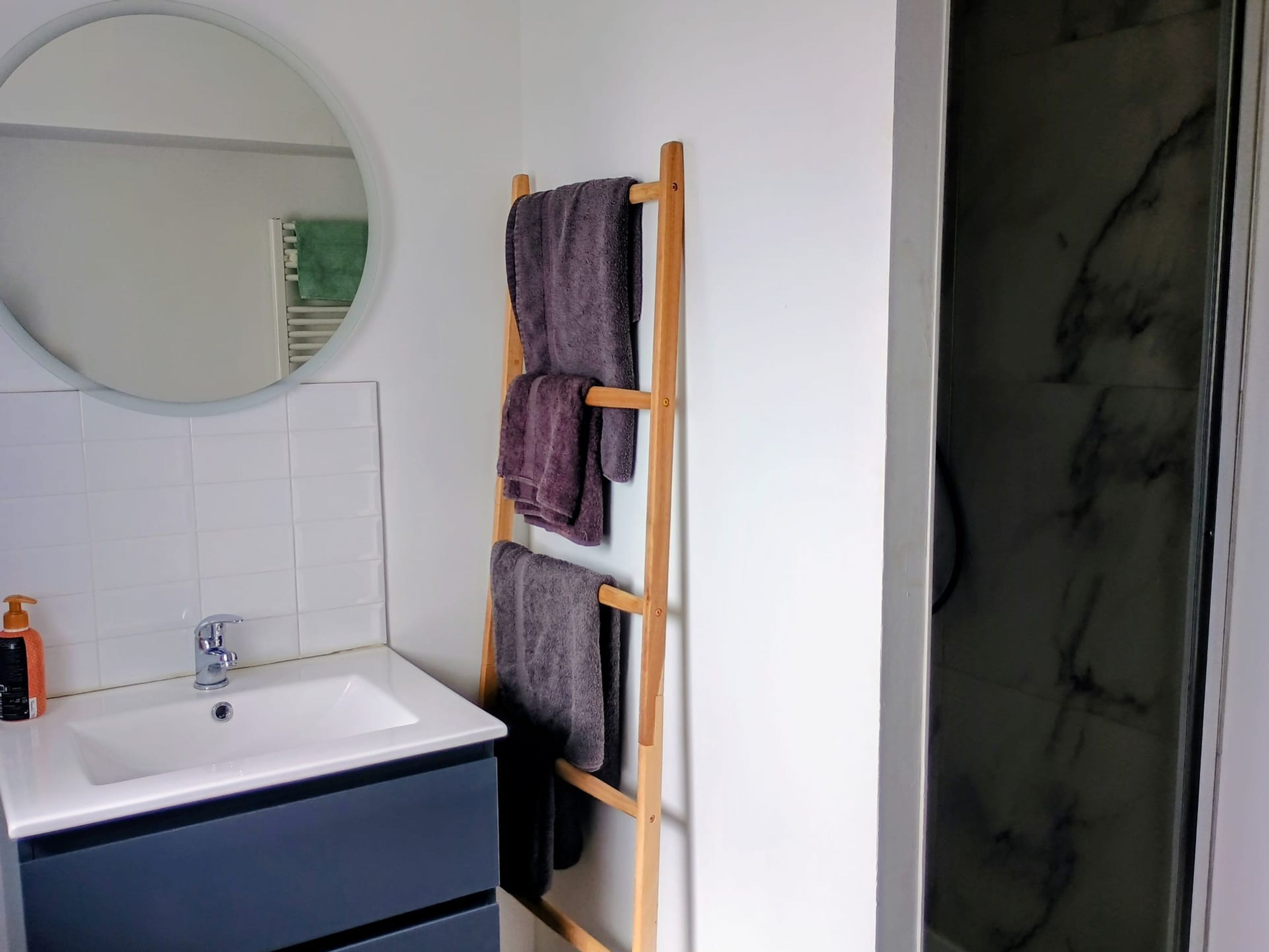 A bathroom with a white sink, a mirror, and a wooden towel rack with several towels.