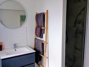 Ein Badezimmer mit einem weißen Waschbecken, einem Spiegel und einem hölzernen Handtuchhalter mit mehreren Handtüchern.