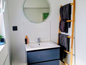 Ein Badezimmer mit weißem Waschbecken, einem Spiegel, einem Handtuchhalter und einer Topfpflanze.