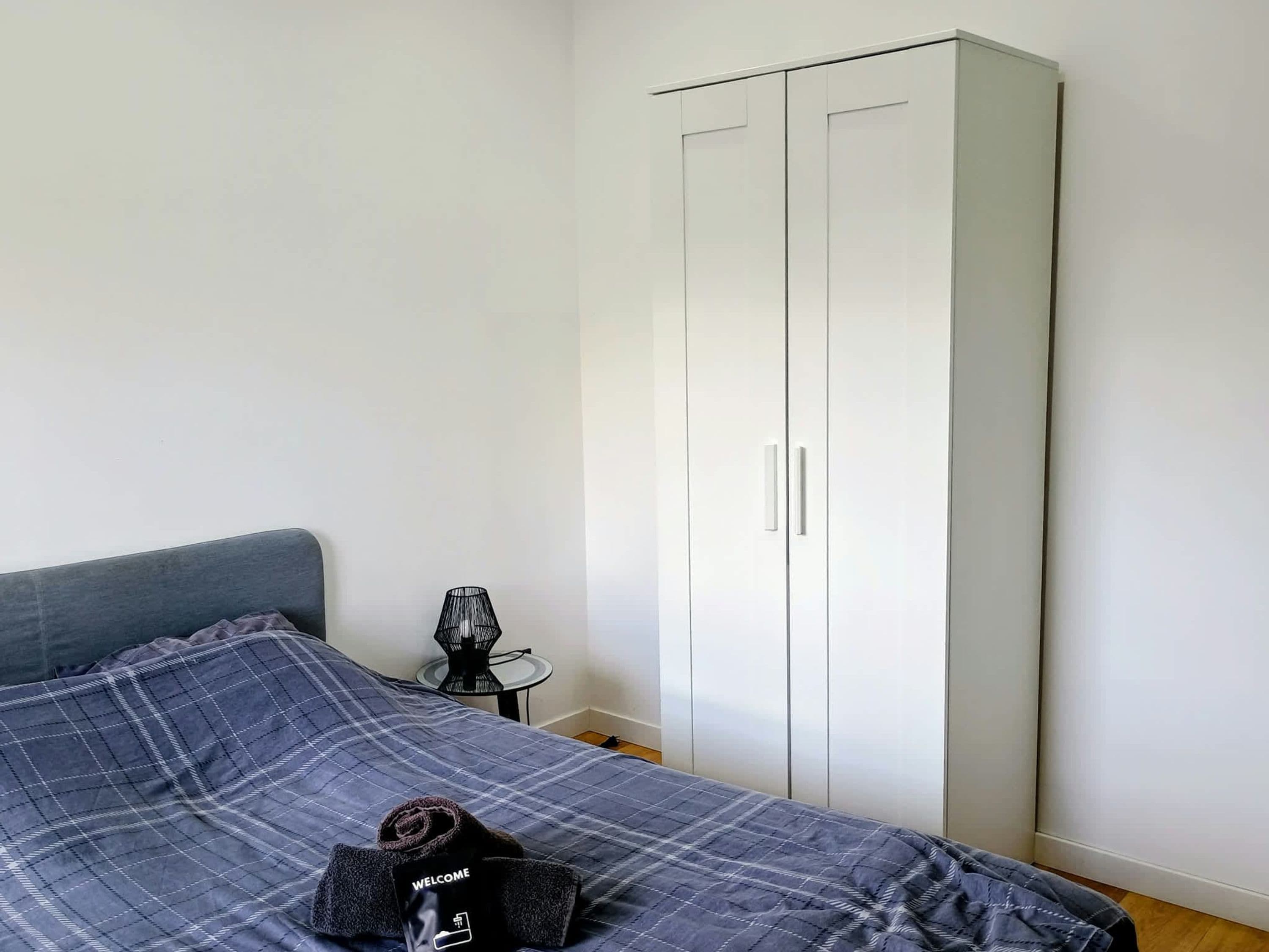 A bedroom with a bed, a wardrobe, and a small table with a lamp.