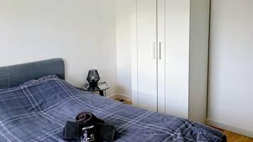 A bedroom with a bed, a wardrobe, and a small table with a lamp.