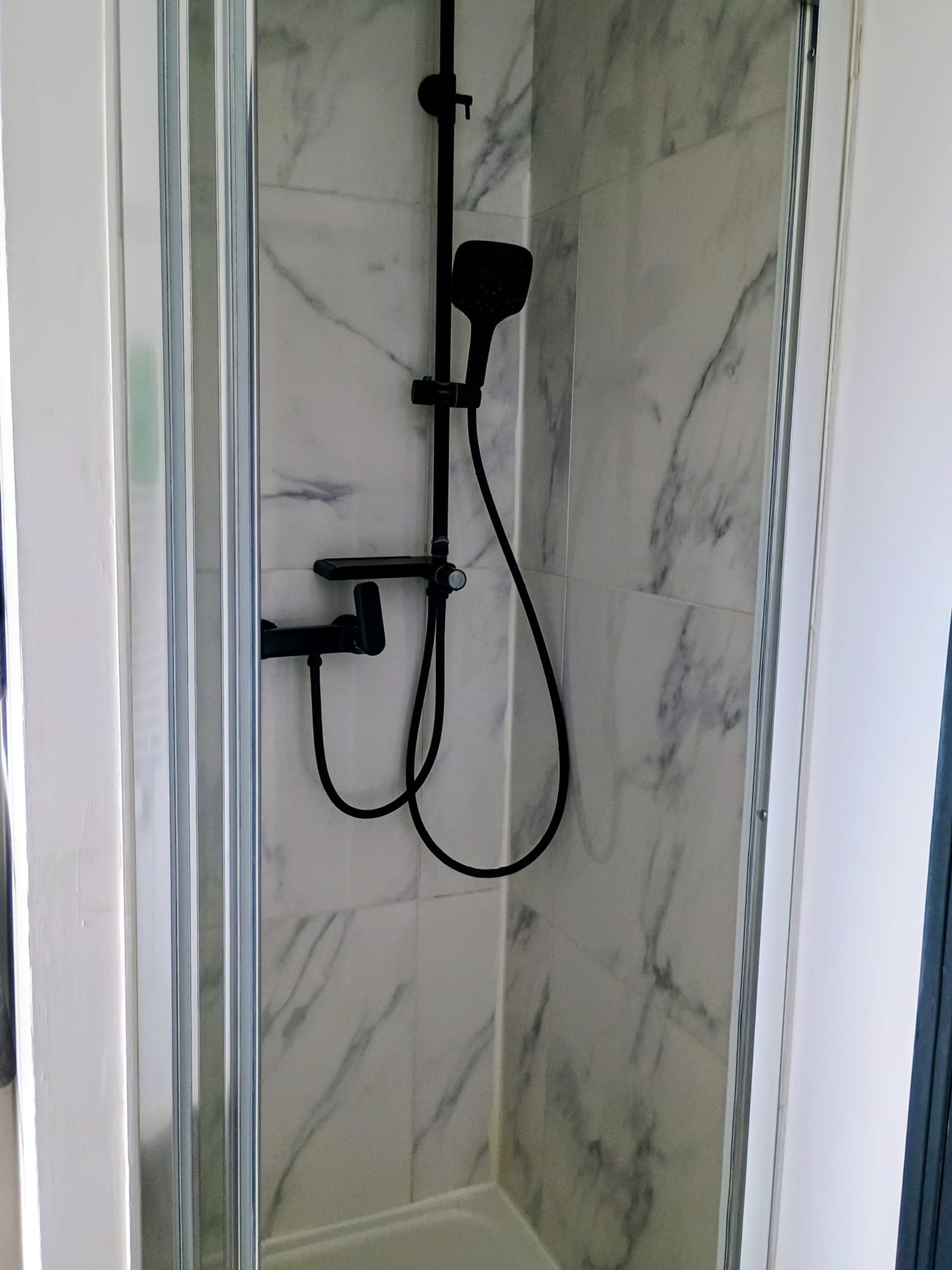 Een douchecabine met een glazen wand, een handdouche en een apart spuitmondje.