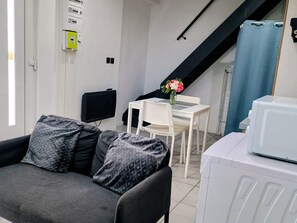 A modern living room with a sofa, a flat-screen TV, a dining table with chairs, and a staircase. - Appartement Tout Confort au Centre Ville de Lens Avec Parking Gratuit (Lens)