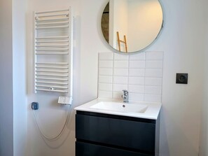 Casa de banho com lavatório branco, espelho, porta-toalhas e parede revestida a azulejos.