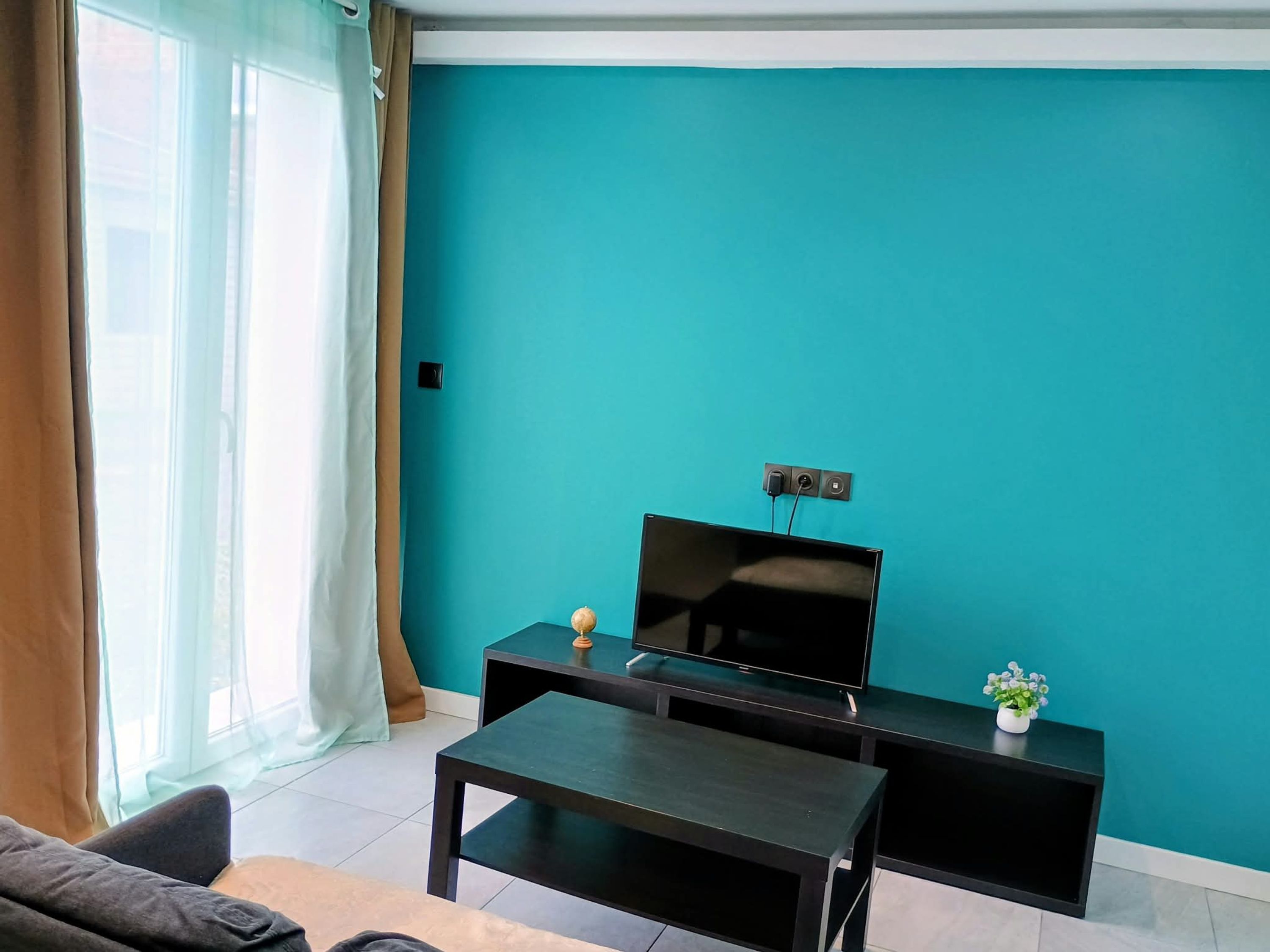 A living room with a flat-screen TV on a black stand, a small table, and a sofa.
