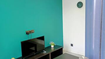 A room with teal walls, a flat-screen TV on a wooden stand, a small globe, and a clock on the wall.