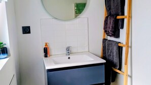 Ein Badezimmer mit weißem Waschbecken, einem Spiegel, einem Handtuchhalter und einer Topfpflanze.