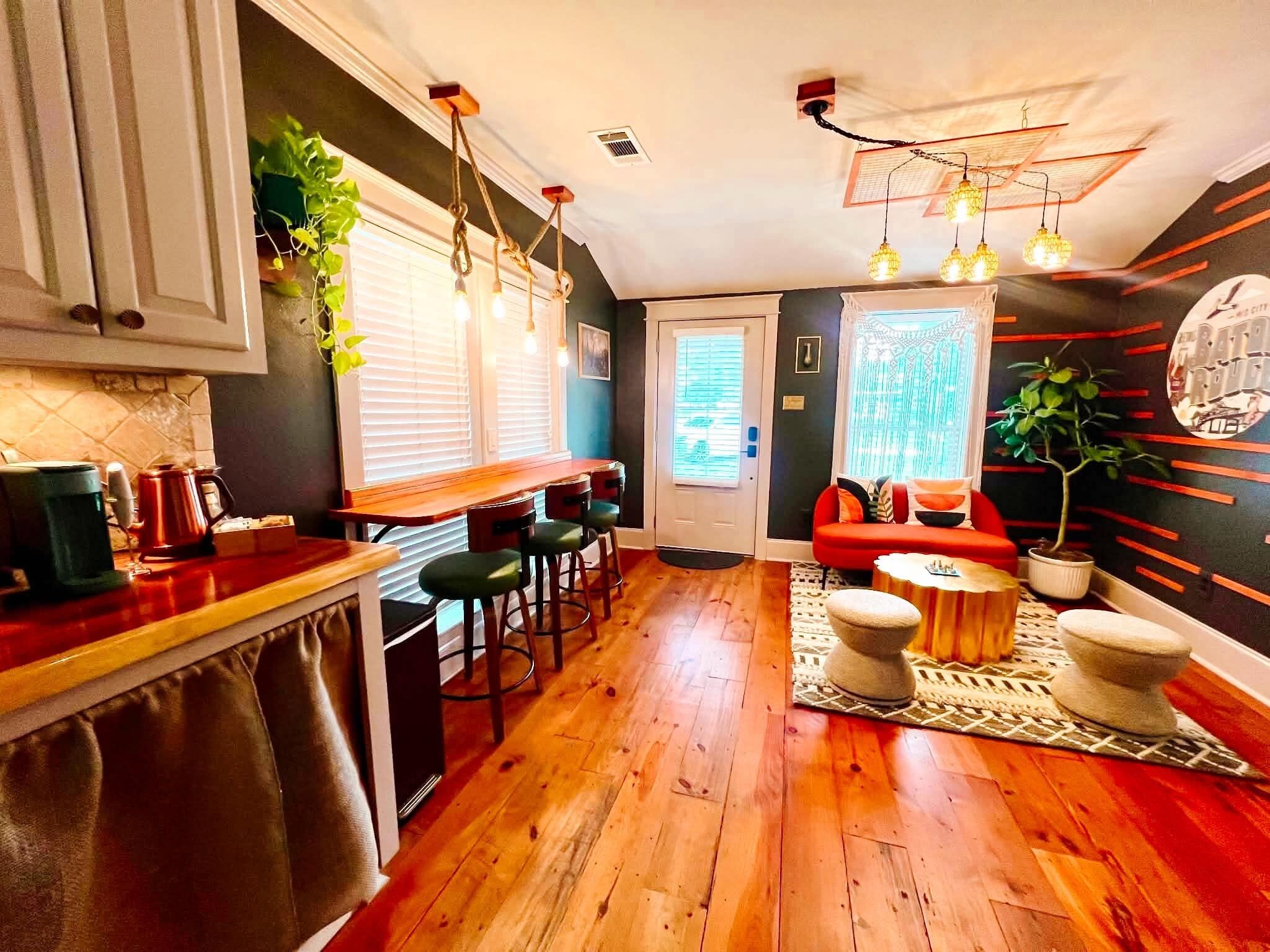 A modern kitchen with wooden flooring, bar stools, and a dining area with a red sofa and coffee table.