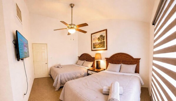 A hotel room with two beds, a ceiling fan, a television, a framed picture, and a window with blinds. - Casa de Huespedes Valles (Ciudad Juarez)