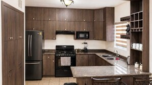 Une cuisine moderne avec des meubles de couleur bois foncé, un réfrigérateur noir, un four à micro-ondes et une cuisinière. On y trouve deux tabourets de bar et une poubelle.