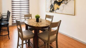 A dining area with a round table, four chairs, a potted plant, and a wall-mounted abstract painting.