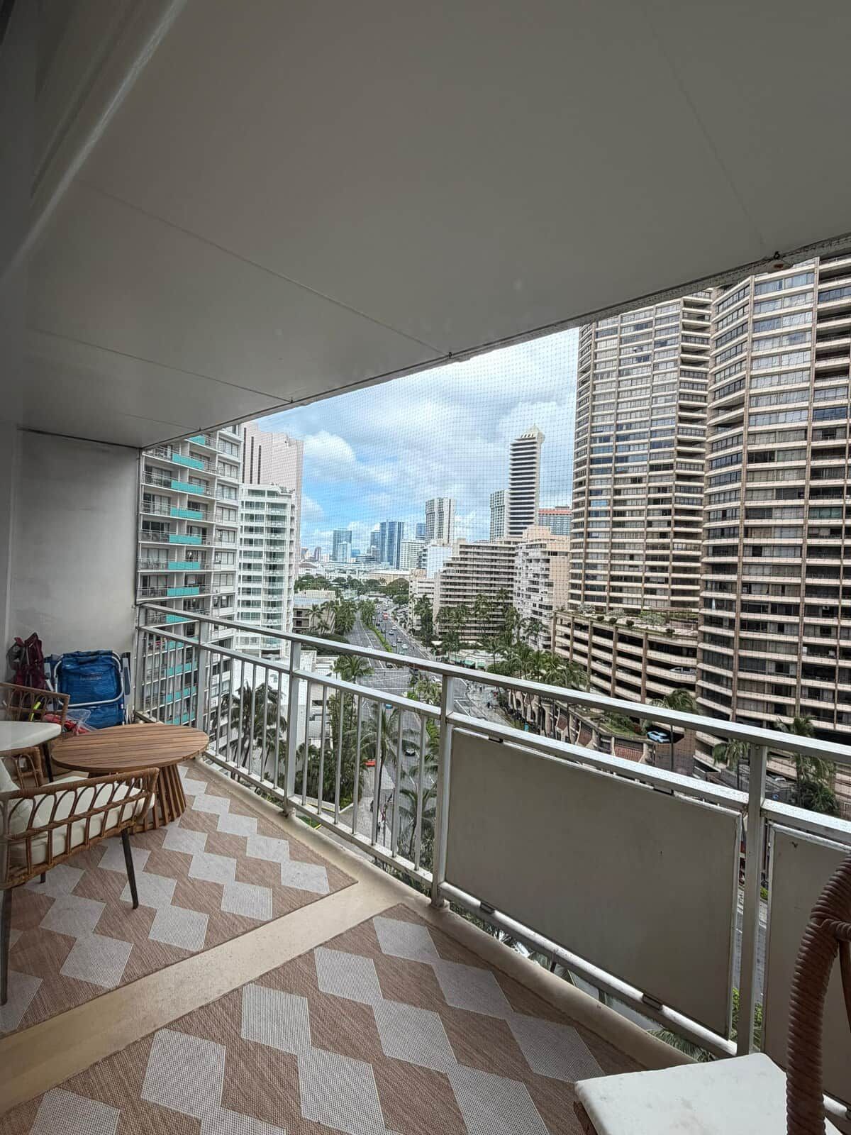 A balcony with a city view, a table, chairs, and a patterned floor.