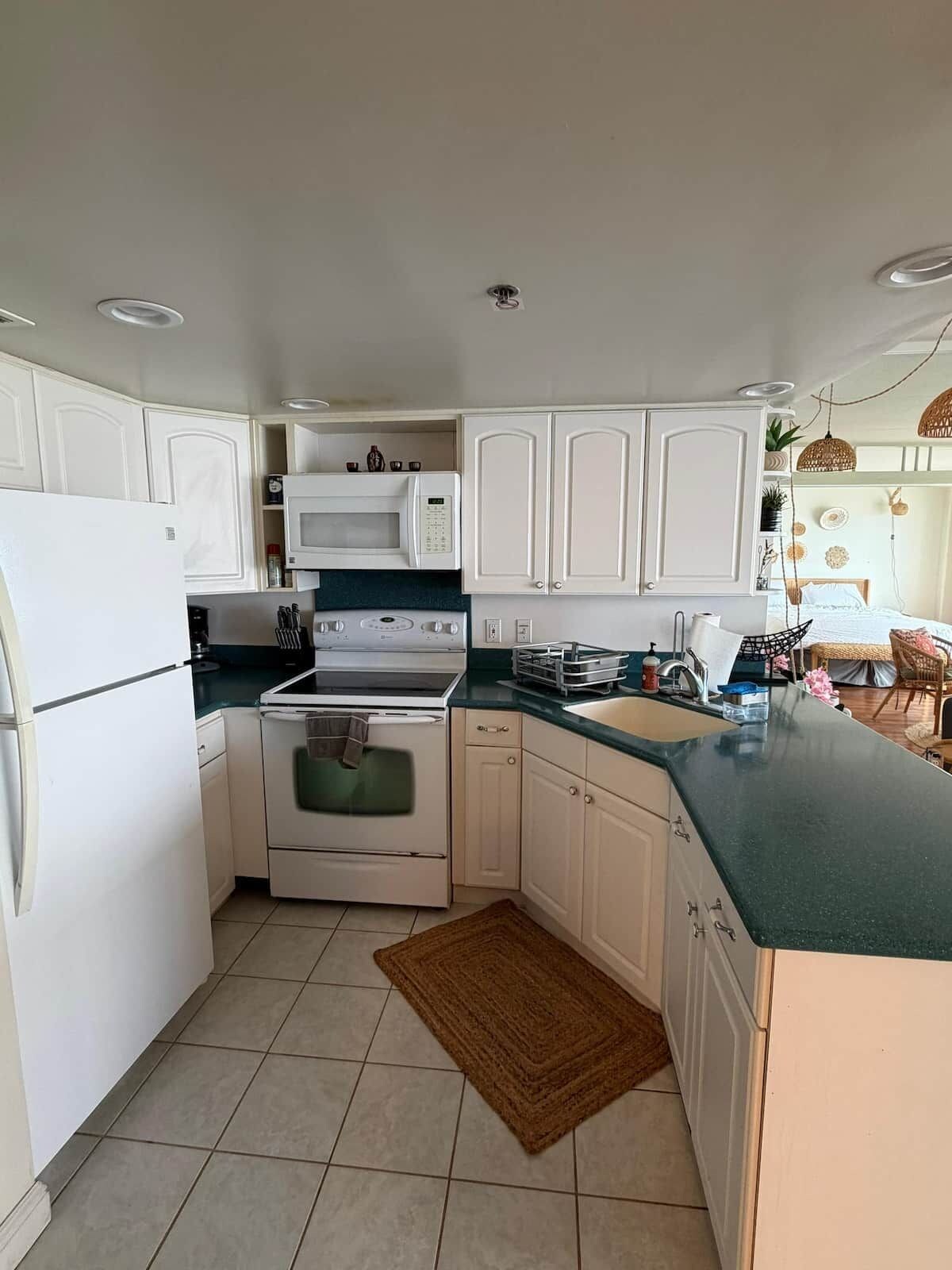 A kitchen with white cabinets, a stove, a microwave, and a sink.