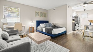 Un dormitorio moderno con cama, mesita de noche, lámpara y vista a la cocina.