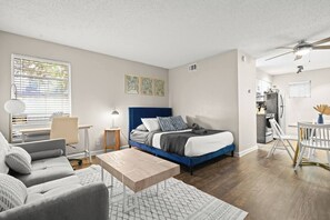A modern bedroom with a bed, bedside table, lamp, and a view of the kitchen. - Austin 2BR Home with 3 Beds & Great Location (Austin)