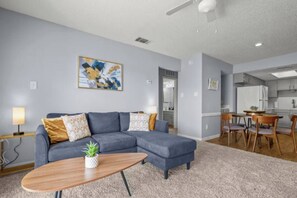 A modern living room with a sectional sofa, a coffee table, and a dining area with a wooden table and chairs. - Austin 2BR Home with 3 Beds & Great Location (Austin)