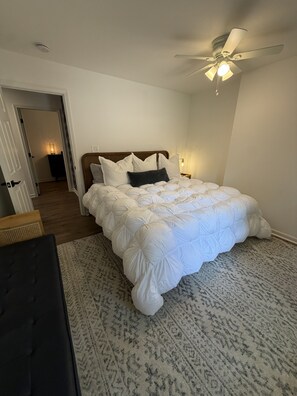 Een slaapkamer met een bed, een plafondventilator, een nachtkastje en een deur naar een andere kamer.