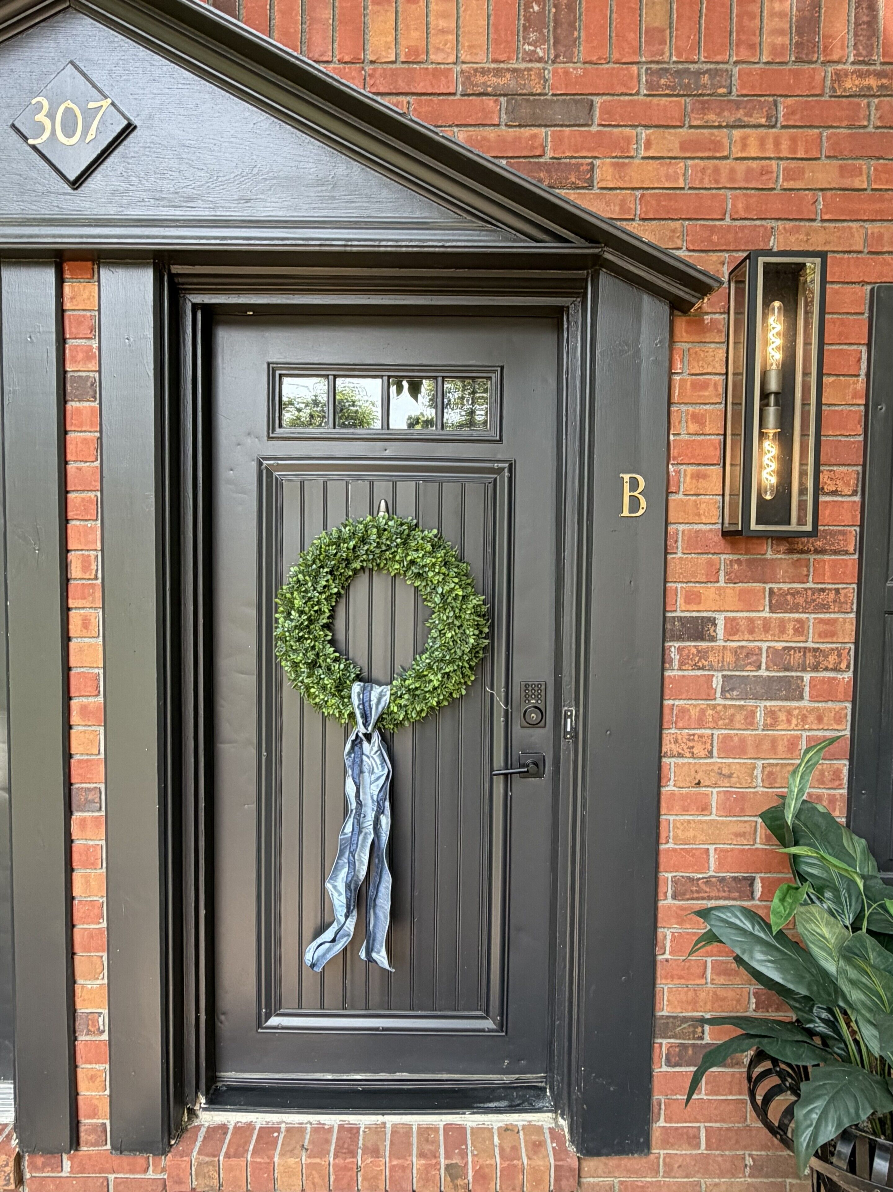 A dark gray door with a number '307' above it, a 'B' on the right, and a wreath with a blue cloth tied around it.