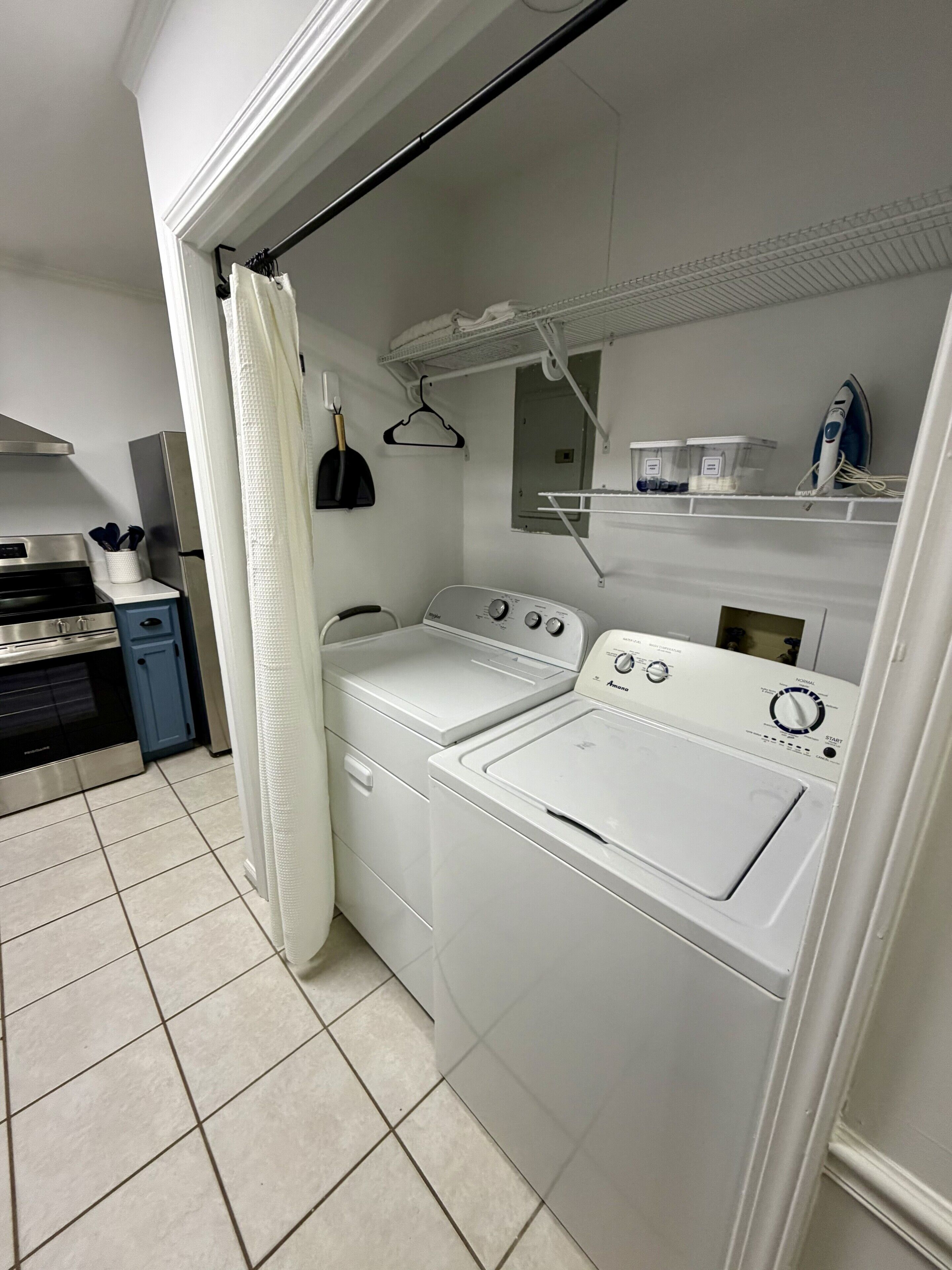 A laundry area with a washing machine and dryer, a drying rack, and a small shelf with containers.