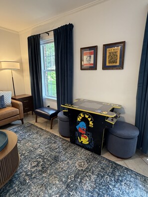Ein Zimmer mit einem Spieltisch, einer Couch, einer Lampe und zwei gerahmten Bildern an der Wand.