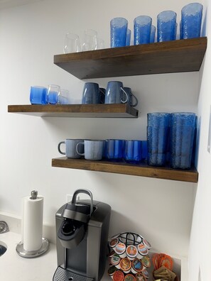 A kitchen with a coffee maker, a paper towel holder, and shelves with blue glassware. - Walk to Square or Campus from 2-bedroom / 2.5 bath condo in charming Oxford (Oxford)