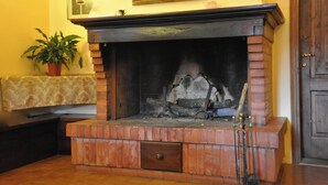 A fireplace with a brick surround, a potted plant, and a framed picture above it. - Homerez - House in Gattaia with pool (Gattaia)
