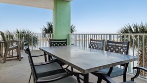 An outdoor patio with a table and chairs, surrounded by a railing, palm trees, and a clear sky. - Hooked Bliss|Bay Views+Boat Slip+Beach Access (Gulf Shores)